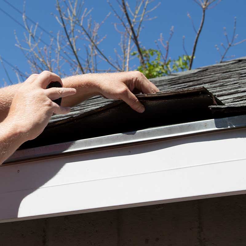 two roofing contractors with yellow hard hats and hammering shingles into a home's roof